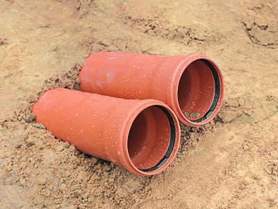 Zwei orangefarbene Rohre, die im Sand liegen.